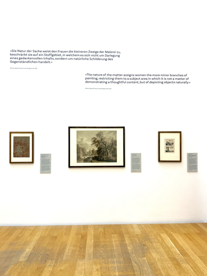 An einer Wand hängen drei unterschiedliche, gerahmte Kunstwerke. An der weißen Wand ist ein Zitat lesbar: »Die Natur der Sache weist den Frauen die kleineren Zweige der Malerei zu, beschränkt sie auf ein Stoffgebiet, in welchem es sich nicht um Darlegung eines gedankenvollen Inhalts, sondern um natürliche Schilderung des Gegenständlichen handelt.«