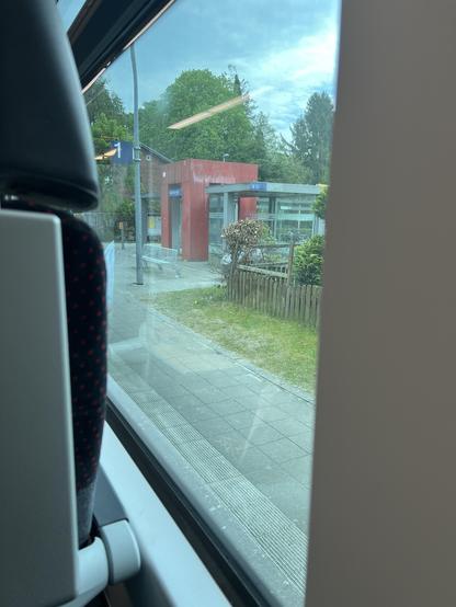 Blick vom halben Wand-Fensterplatz - das Fenster beginnt erst ca. 20 cm vor mir - auf den Bahnsteig in Gelbensande. Draußen ist ein Wartehäuschen im typischen DB-Design der 90er Jahre zu sehen, mit rotem, etwas beschmierten Mittelteil und Glasteilen an beiden Seiten.
