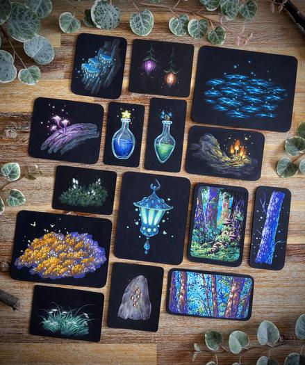 A photo of 15 small original paintings on black paper, placed on a wooden table and surrounded by leaves and branches for decoration. The paintings feature different nature and fantasy motifs, such as glowing mushrooms and plants, vibrant moss, little forest scenes, lanterns, magic potions,… All paintings have rounded corners.