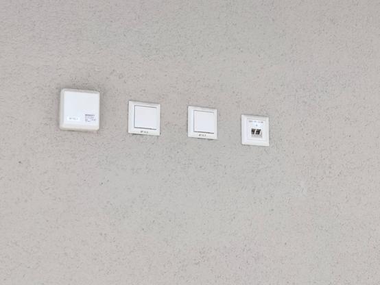 Eine verputzte Außenwand, an welcher verschiedene Anschlussdosen (Strom, Netzwerk, etc.) nebeneinander angebracht sind