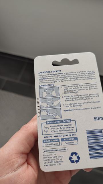 Foto. Rückseite der Zahnseideverpackung.  Anhand einer frei im Raum schwebenden Zahnreihe wird illustriert, wie die Zahnseide zu benutzen ist. 