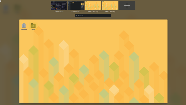 Imagen de un escritorio virtual mostrando un fondo amarillo con un patrón de cubos isométricos en tonos amarillos, azul claro y verde claro. En la parte inferior izquierda se ven dos iconos: una papelera y una carpeta etiquetados como "Papelera" e "Inicio", respectivamente. En la parte superior, hay miniaturas de otros escritorios y un botón "+" para añadir uno nuevo, con un buscador debajo.