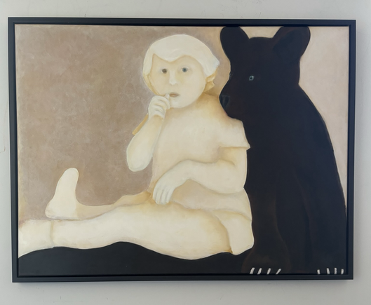 A small child sits on a rug while a bear cub leans against her. 
