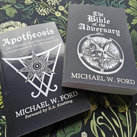 Twee boeken van Michael W. Ford liggen op een met plantenpatroon bedekte ondergrond. Links ligt het boek "Apotheosis: The Ultimate Beginner’s Guide to Luciferianism & the Left-Hand Path" met Lucifer's Sigil op de kaft. Rechts ligt "The Bible of the Adversary" met een afbeelding van Baphomet op de kaft.