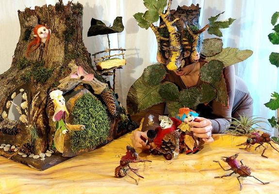 Die Märchenerzählerin Sandra Lienhard verkleidet mit einer Baum-Gesichtsmaske. Sie führt kleine Puppen aus Holz und Tannenzapfen über eine Fantasielandschaft.