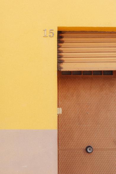 Detail photograph of the upper corner of an industrial door and its shutter. The door and shutter are brown and ochre, and the wall is yellow and cream. The number 15 can be seen next to the door.