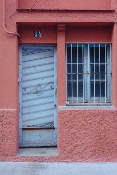 Photograph of the facade of a house painted salmon-red with a chalk-blue door and windows. The number 34 can be seen above the door.