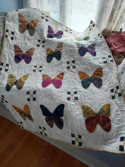 a quilt, it is 4 rows of 3 butterflies, all of them a different hand-dyed color scheme, a wavy line and small box of blocks separating each one 
