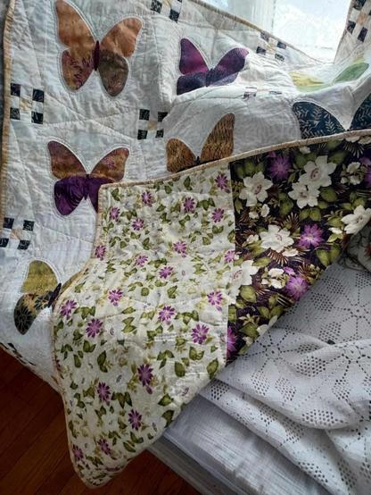 the quilt with the corner turned up, showing the purple and green on white floral backing of it 