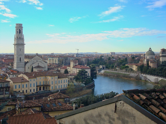 A river cuts through the city of Verona in Italy. What looks like a church sits amid other buildings on the left bank and more buildings and trees are on the right 