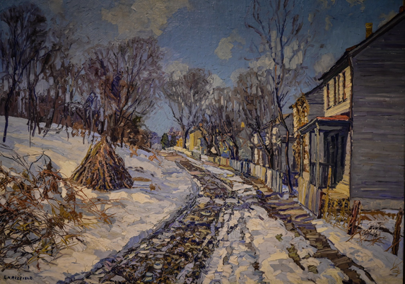 a painting of a dirt road. tracks  from wheels ,  silver-brown, snow on either side and up the middle, some small houses on the right side, leafless trees around, the sky blue with white clouds in it 