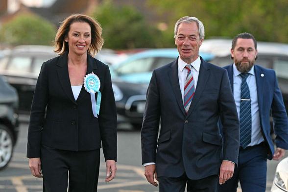 Nigel Farage looking like he just crapped his pants and a bearded guy walking behind Farage looking weirdly 