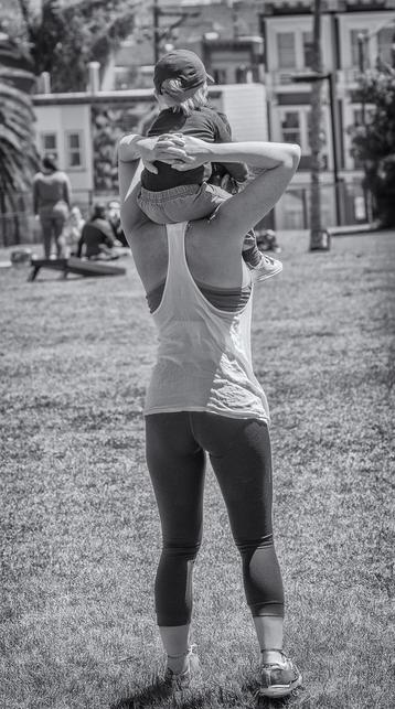 Mom carries child on her shoulders in a park in San Francisco.