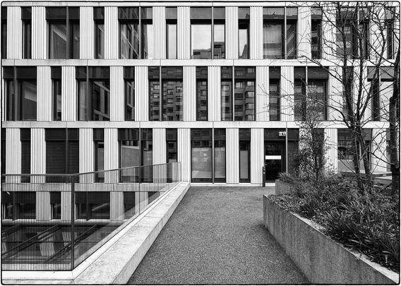 Schwarzweissfotografie mit einer Fensterfront, in der sich die gegenüberliegende Fensterfront spiegelt. 