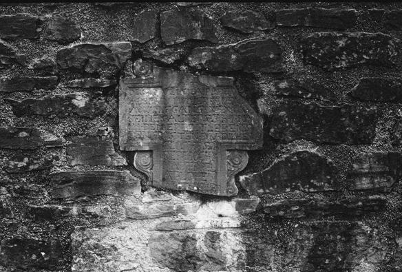 Black and white photo of a fragment of a 17th century gravestone embedded in a medieval wall