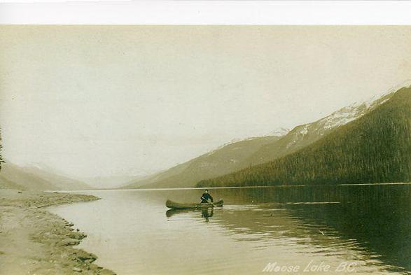 A man in a canoe paddles across a long thin lake. The image is not, however, of Stuart's Lake on which Fort St James sits.