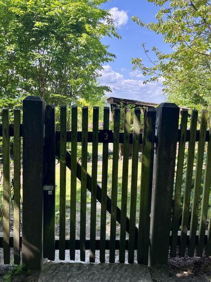 Das hölzerne Gartentürchen mit einem Kleingarten dahinter.