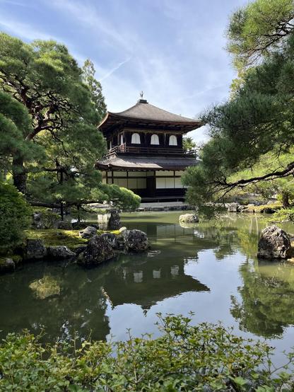 Un pequeño templo de base cuadrada y un par de alturas asoma entre los árboles de hojas verdes al fondo de un pequeño estanque en el que se refleja. Día soleado y cielo azul. Pese al nombre de «pabellón de plata», las paredes son blancas o de madera oscura. Al parecer, debido a guerra civil, no pudo recubrirse el edificio con plata tal y como se había planeado inicialmente.