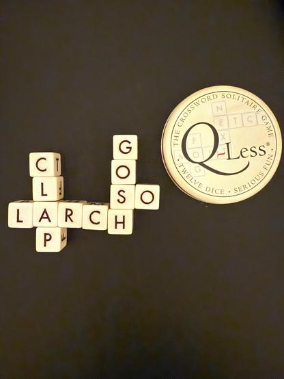 The image features letter tiles arranged to form the words "CLAP”, “LARCH", “SO” and "GOSH", alongside a round game tin labeled "Q-Less: The Crossword Solitaire Game." The background is dark, highlighting the tiles and the game tin.