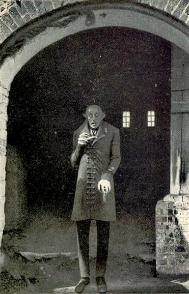 Max Schreck in a promotional still for the film

 Created by F. W. Murnau (died 11 March 1931), Henrik Galeen (died 30 July 1949) and Fritz Arno Wagner (died 18 August 1958).

Nosferatu promotional image.

Max Schreck appears in full costume as the grotesque, vampiric Count Orlok. His appearance is haunting: a bald, bat-like figure with elongated fingers, pointed ears, a gaunt face, and wide, predatory eyes that evoke a sense of unease and dread.

He stands frozen in a dramatic, hunched pose, his clawed hands extended as if reaching toward an unseen victim. His expression is blank yet menacing, emphasizing his unnatural, undead presence.

The image is starkly lit, with high contrast between deep shadows and pale highlights, emphasizing Orlok’s cadaverous complexion and angular features. The atmosphere is tense and gothic, rooted in German Expressionist style, which used distortion and shadow to evoke psychological horror.

https://en.wikipedia.org/wiki/Nosferatu#/media/File:Schreck.jpg