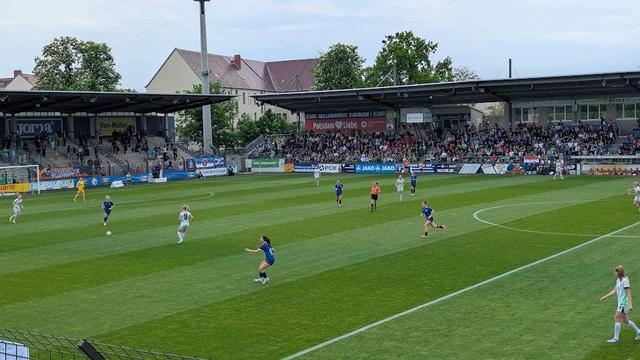 Blick auf ein Fußballfeld. Spielerinnen in blauen und weißen Trikots in Bewegung.
