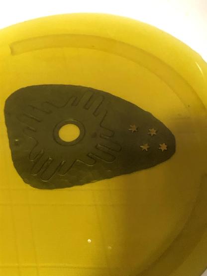 The image features a dark object in a yellow liquid. The object has a circular hole and is decorated with four small star shapes.