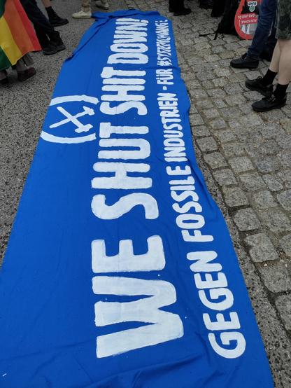 Blaues transparent auf dem Boden, "we shut shit down - gegen fossile Industrie - für #SystemChange!" Mit Logo von Ende Gelände