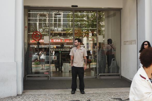 Trabalhador de um supermercado de uma grande cadeia observa o desfile à frente da loja, durante uma pausa para o cigarro