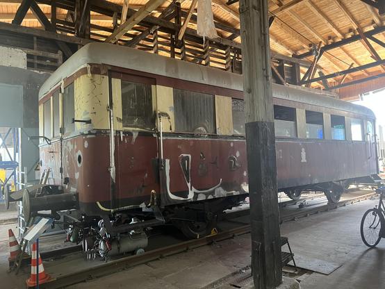Rot-beiger Beiwagen im Lokschuppen, ohne Scheinwerfer mit leichten (sichtbaren) Rostspuren und teilweise abgeblättertem Lack.