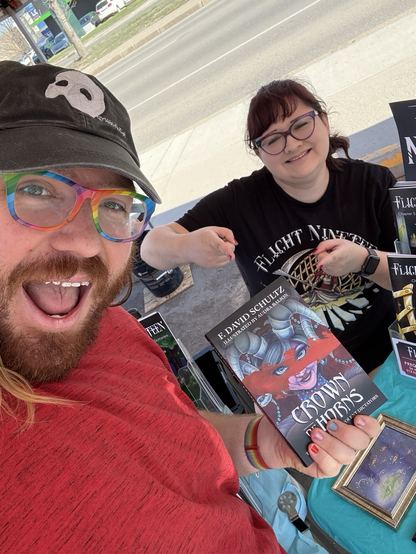 A pair of smiley folk pose for a selfie with the book Crown of Horns. 