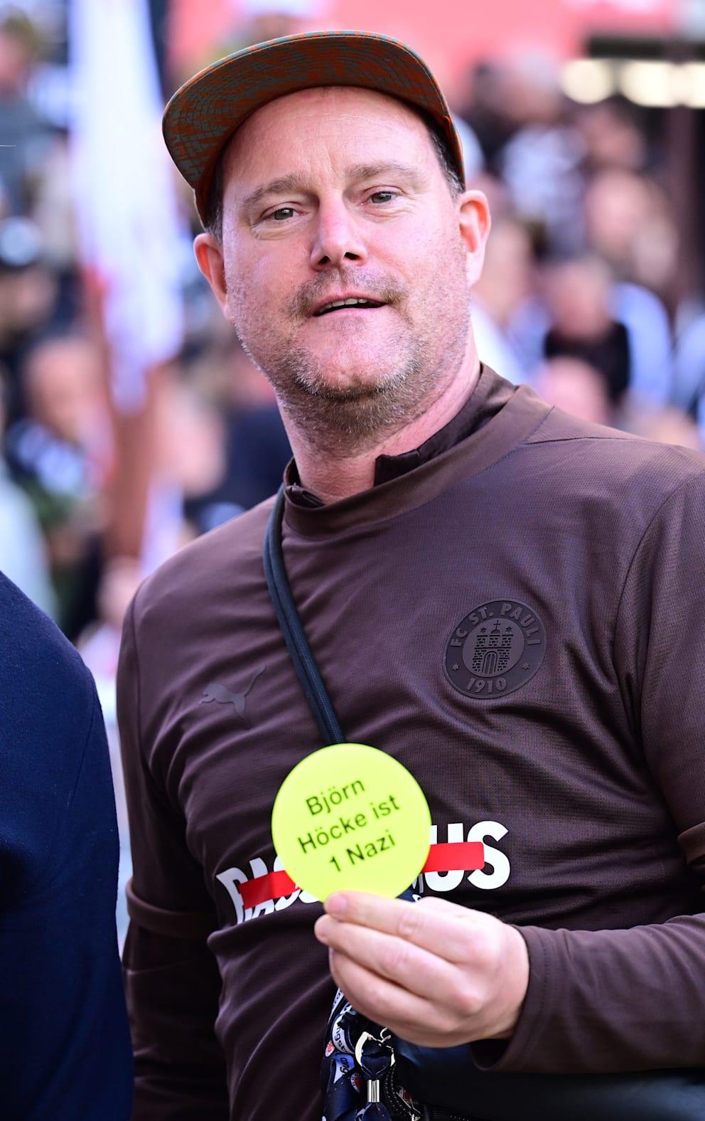 Der Trainer hält einen runden, gelben Aufkleber in die Kamera, auf dem steht: Björn Höcke ist ein Nazi. Der Trainer hält einen runden, gelben Aufkleber in die Kamera, auf dem steht: Björn Höcke ist ein Nazi.