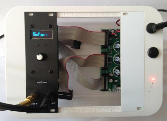 Photo of my cake-box Eurorack enclosure with a black MiniDexed Eurorack module installed showing "Srings 1" on the display as it is running my picoDexed code.