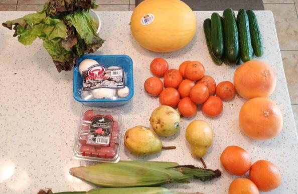 The array of items includes lettuce, a sweet melon, big pile of mini cucumbers, mushrooms, cherry tomatoes, grapefruit, two kinds of oranges, corn on cob, and pears.