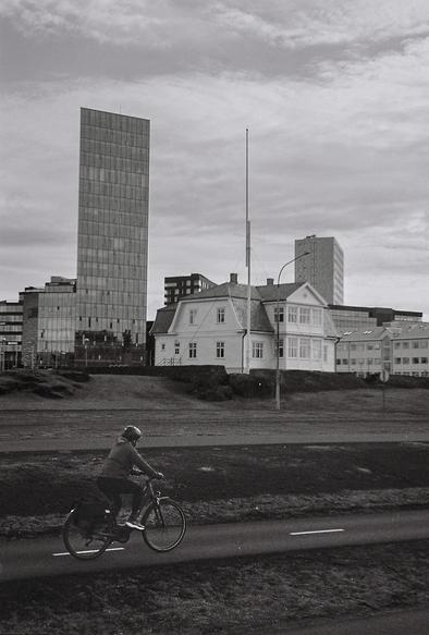 Black and white picture of the house Hofdi. In the foreground isa person passing by on a bike.