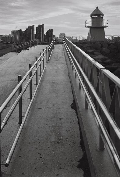 Black and white picture of a lighthouse in Reykjavík. Inthe distance are tall buildings.