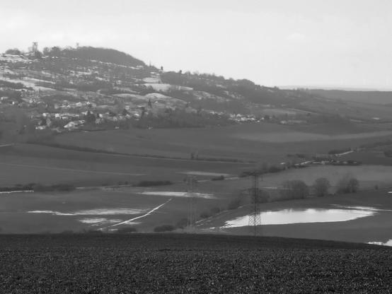 Paysage de vallée en noir et blanc, sur la colline au fond reste par endroits une mince pellicule de neige