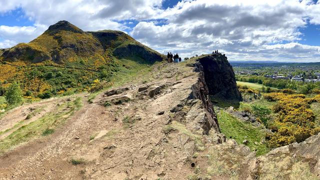 The tip of Salisbury Crags jutting out, extinct volcano Arthur’s Seat in the background covered in blooming gorse flowers, more blooming gorse down below