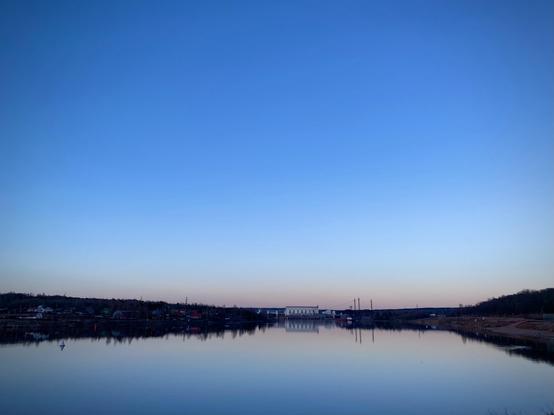 River landscape: river bank with houses, sky reflected in water.