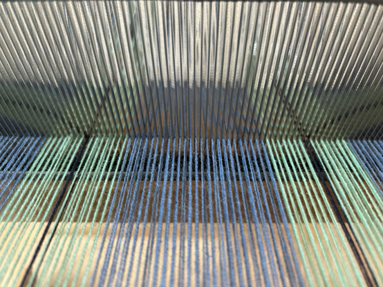A close up look at warp threads passing through the reed of a hand loom 