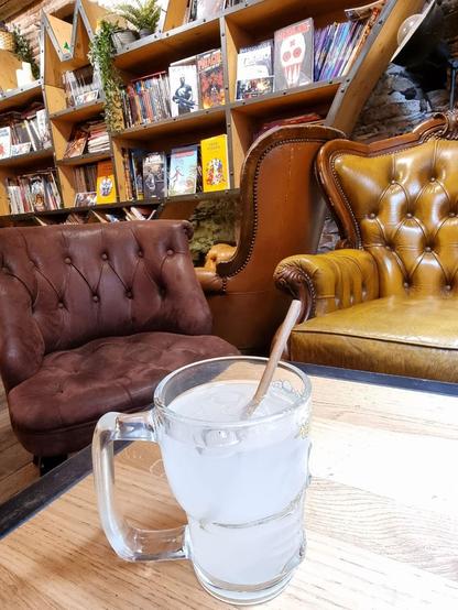 A glass of ginger beer on a table in a swanky looking library with a big bookshelf of comics in the background