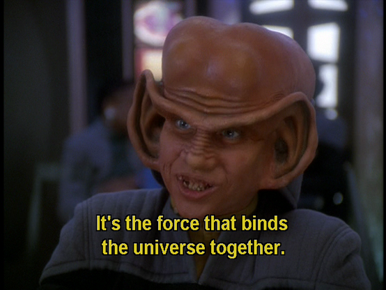 Star Trek Deep Space Nine scene. Nog is pictured up close and in Starfleet uniform in Quark's bar. He's a Ferengi, and has giant ear lobes significantly bigger than a humans and the top curve of the ear extends and connects across like a unibrow. Also from the front, his bald head is kind of shaped like a beluga whale. He's explaining something here with enthusiasm. Closed caption reads, "It's the force that binds the universe together."