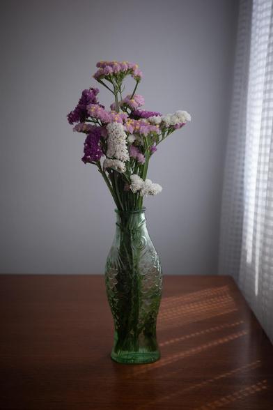 1 - Original picture. Photograph of a fish-shaped pot filled with colorful flowers on a wooden table, with sunlight filtering through the curtains. The scene is slightly underexposed.