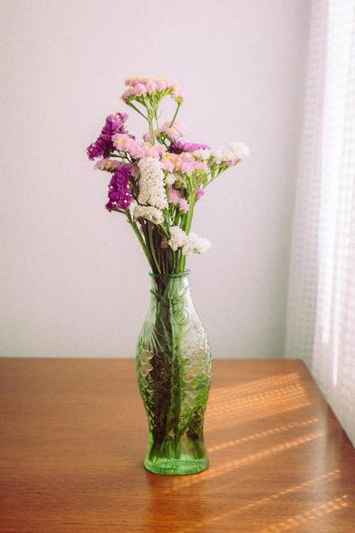 3 - Portra 400 wannabe preset. Photograph of a fish-shaped pot filled with colorful flowers on a wooden table, with sunlight filtering through the curtains. The scene is well lit and has a slight green tint.