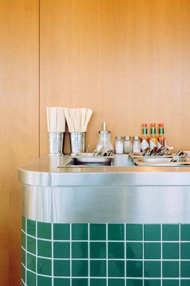 1 - Digital. Photograph of the corner of a counter in a restaurant with chopsticks, a sugar bowl, several salt shakers, and bottles of hot sauce.