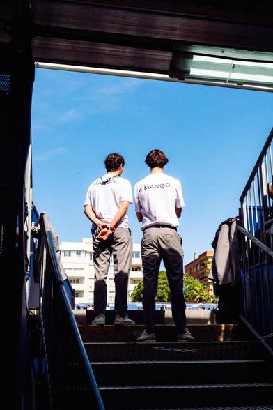 1 - Digital. Photograph of two people at the end of the stairs leading to the stands of a tennis court.