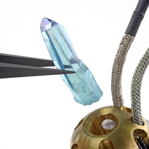Nylon Tipped Tweezers holding a small blue crystal over its brass housing.
