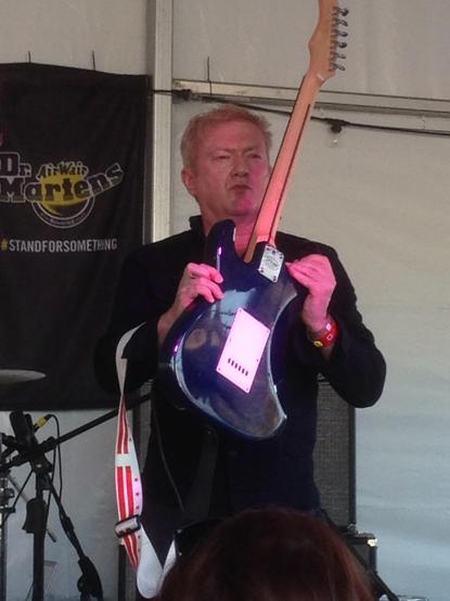 A stern-faced Andy Gill holding his guitar up to produce feedback at SXSW 2015. 