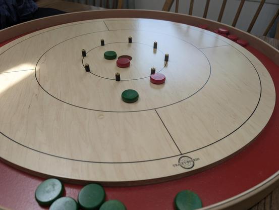 Red gutter Tracey Crokinole board with tan playing area and red and green discs laying about