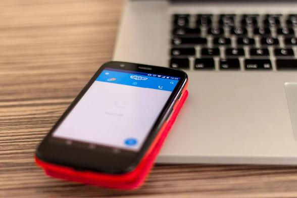Ein Smartphone mit Skype-App, auf einem Laptop liegend. 