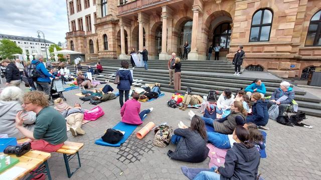Menschen sitzen oder liegen auf Isomatten vor dem Wiesbadener Rathaus. 
